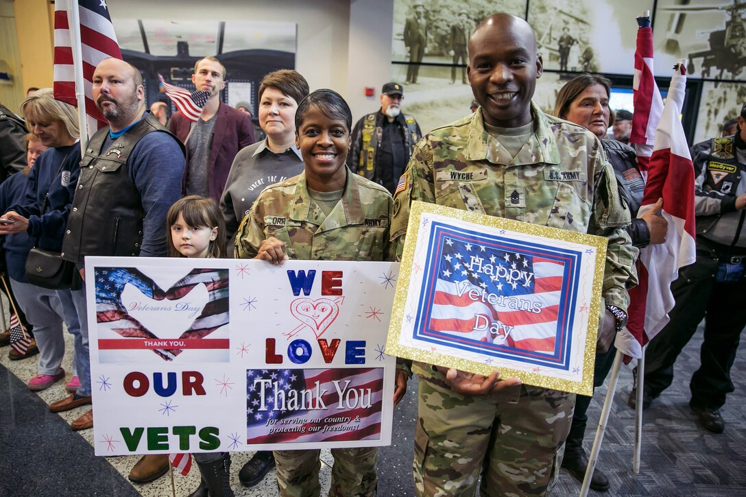 Soldiers and children hold signs welcoming wounded warriors at an airport.