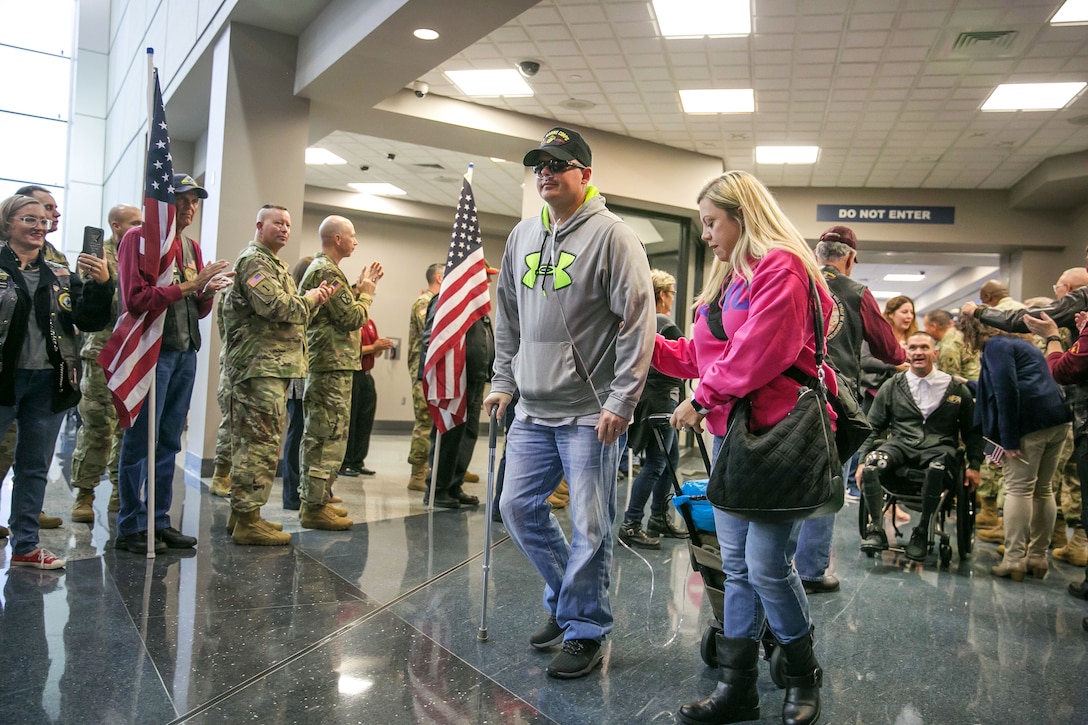 A wounded warrior walks through an airport as people applaud.