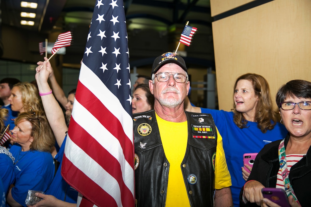 A Vietnam veteran holds the U.S. flag while welcoming wounded warriors.