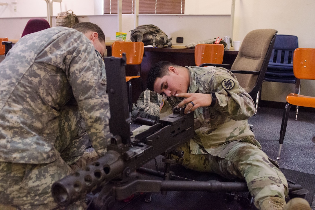 Two soldiers sit on the floor and disassemble a machine gun.