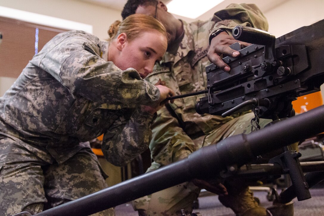 Two soldiers kneel on the ground with a machine gun.