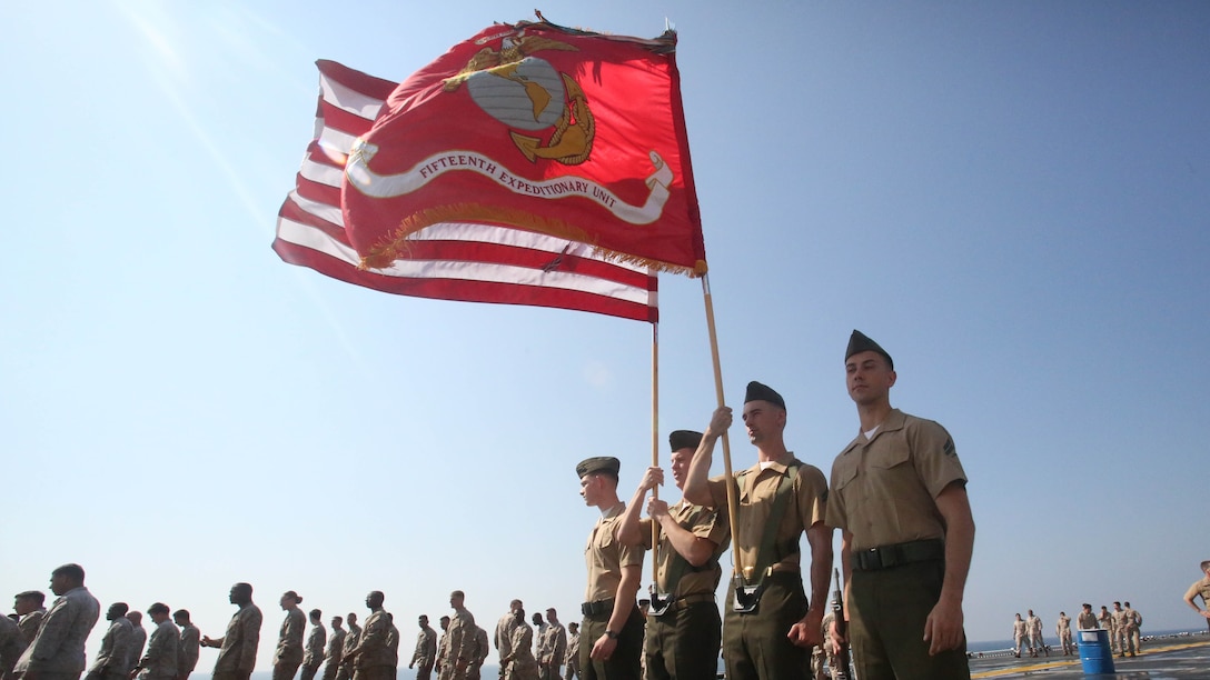 Marines assigned to the 15th Marine Expeditionary Unit aboard the amphibious assault ship USS America (LHA 6) parade the colors on the flight deck during a celebration of the 242nd birthday of the Marine Corps.