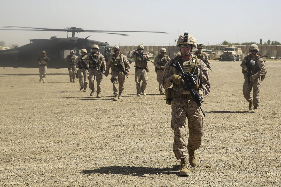 Marines carry weapons as they depart a helicopter before a meeting.