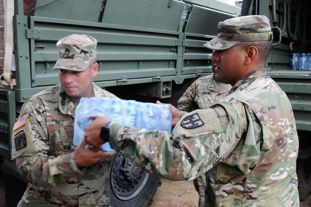 Soldiers unload trucks filled with water and food.