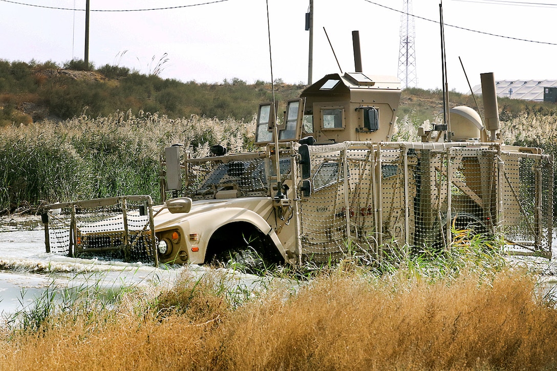 A soldier drives a mine-resistant, ambush-protected vehicle through a water obstacle during a master driver training course.