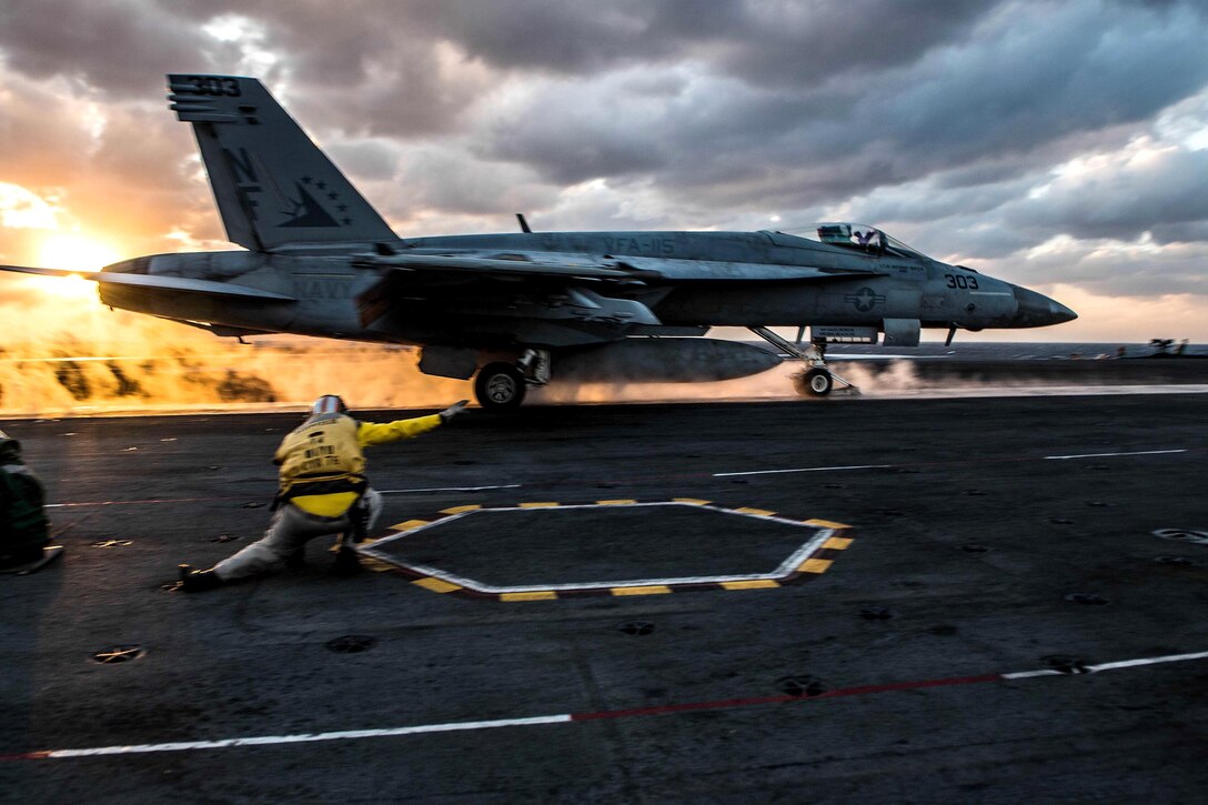 A sailor gives a signal while a jet takes off from an aircraft carrier.