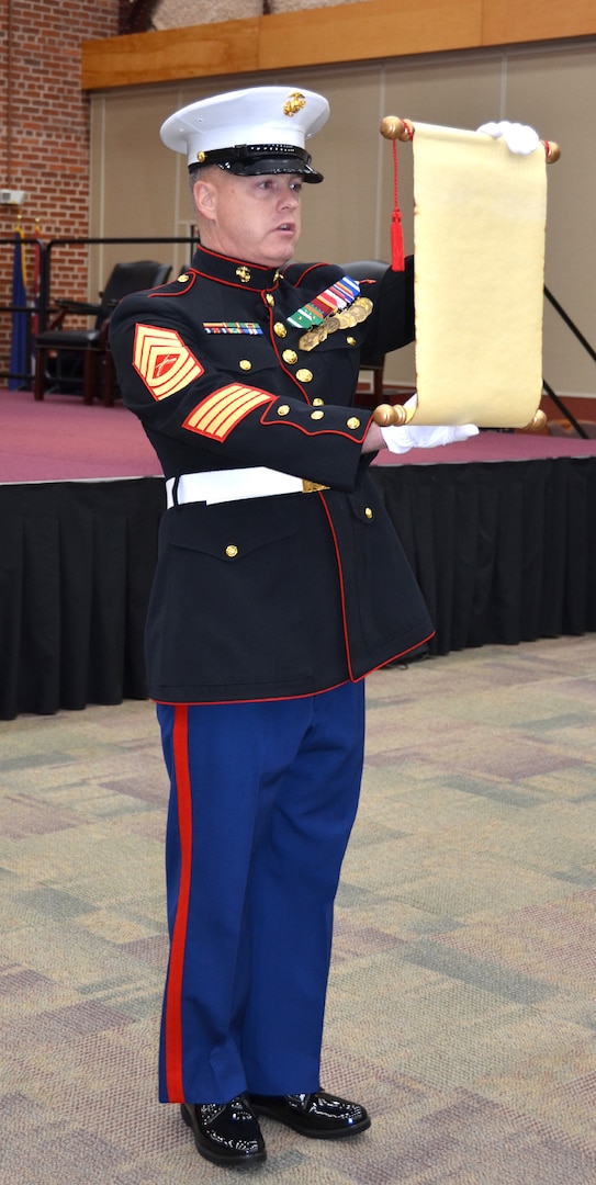 A Marine dressed in his blues reads from a scroll.