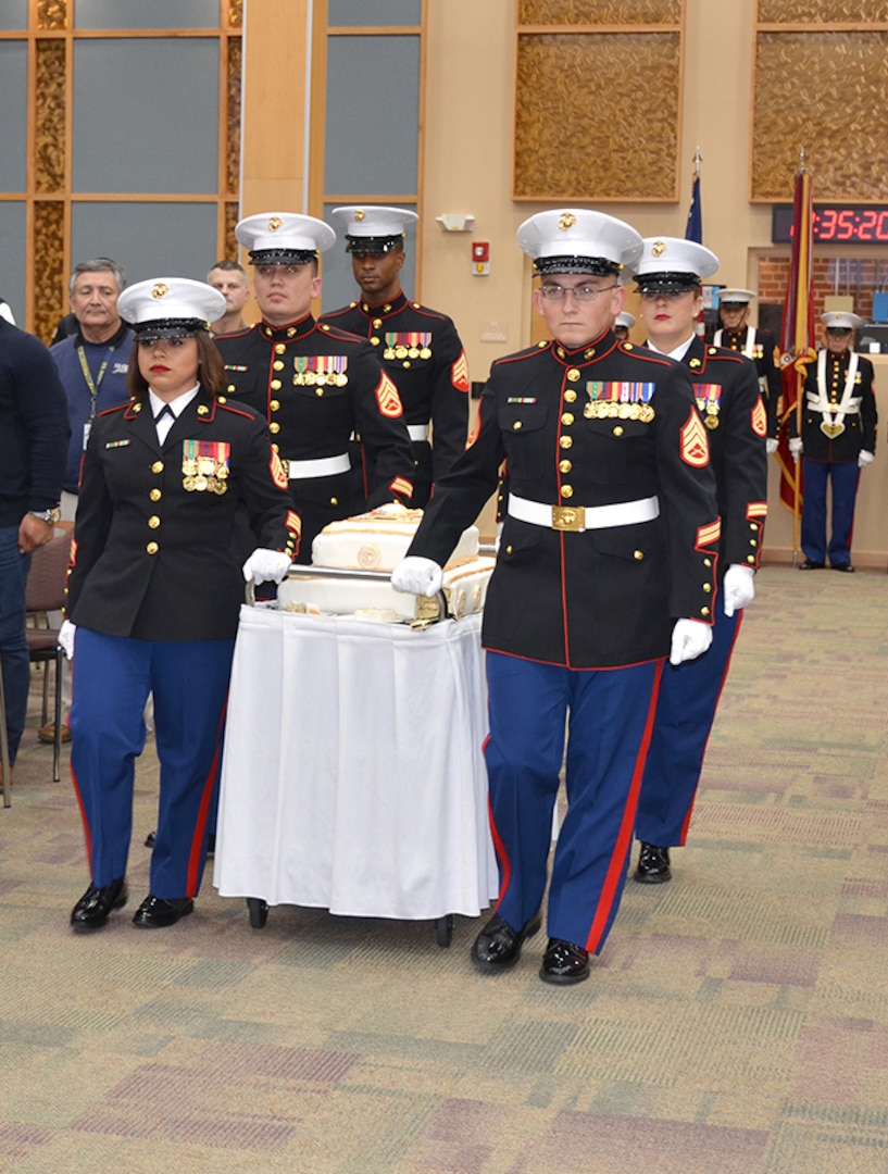 Four Marines roll a cart with a cake into a conference center.