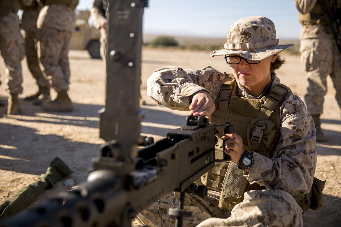A marine sits on the ground operating a machine gun.