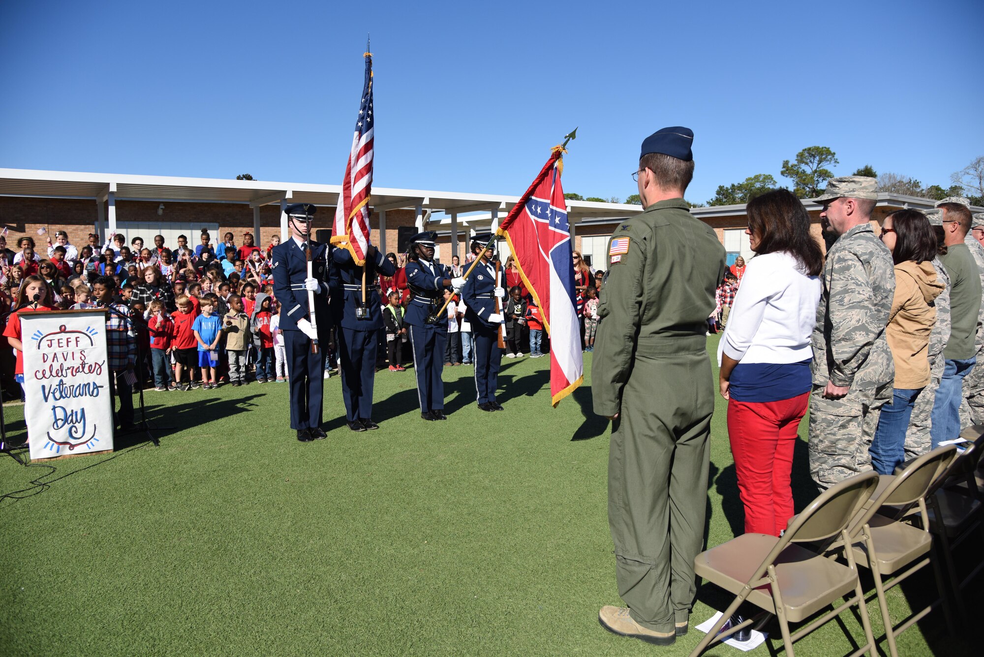 Col. C. Mike Smith, 81st Training Wing vice commander, and fellow audience members honor the flag during the Jeff Davis Elementary School Veterans Day celebration Nov. 10, 2017, in Biloxi, Mississippi. During the event, students recited the Pledge of Allegiance and sang several patriotic songs. Keesler Air Force Base leadership, honor guardsmen and base personnel attended the event. (U.S. Air Force photo by Kemberly Groue)