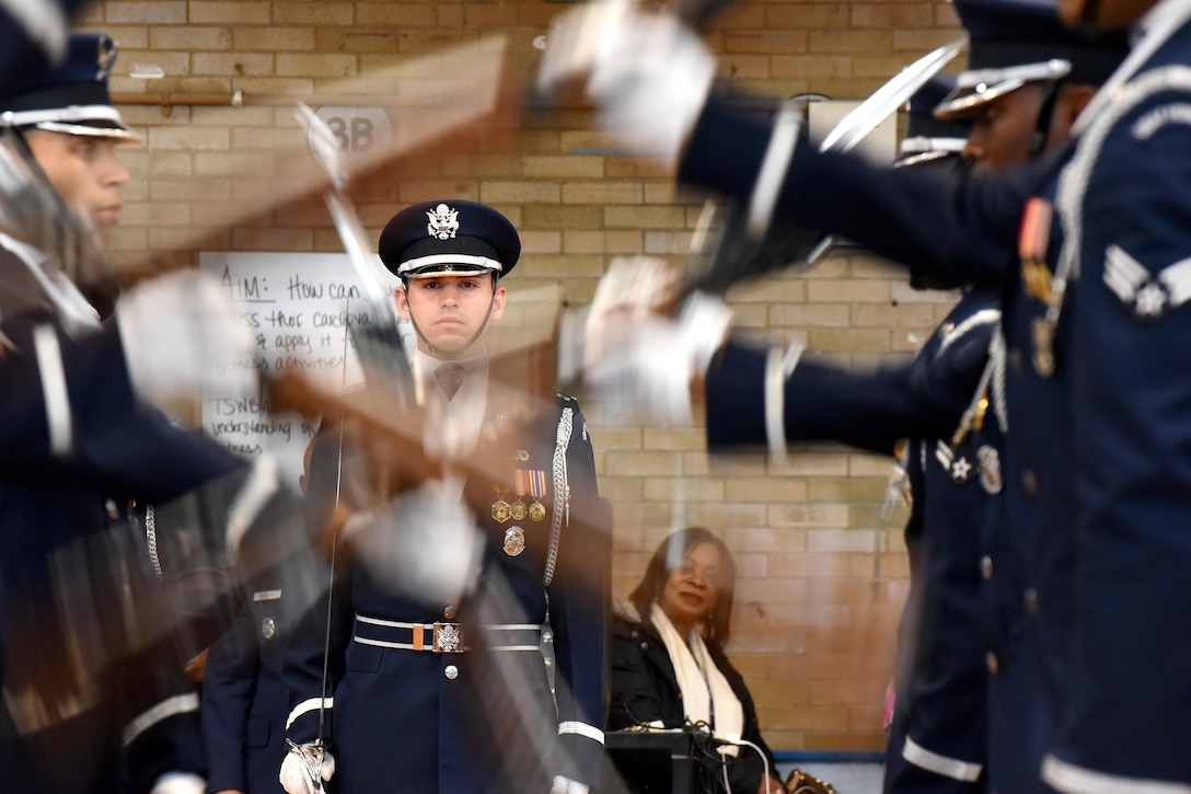 An airman stands in place between two rows of airmen flinging rifles.