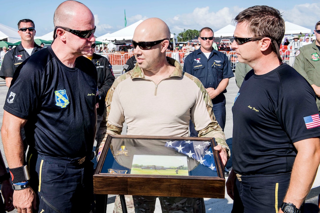 Congressman Brian Mast, center, presents a shadow box in remembrance of Navy Petty Officer 1st Class Remington Peters to members of the U.S. Navy parachute team.