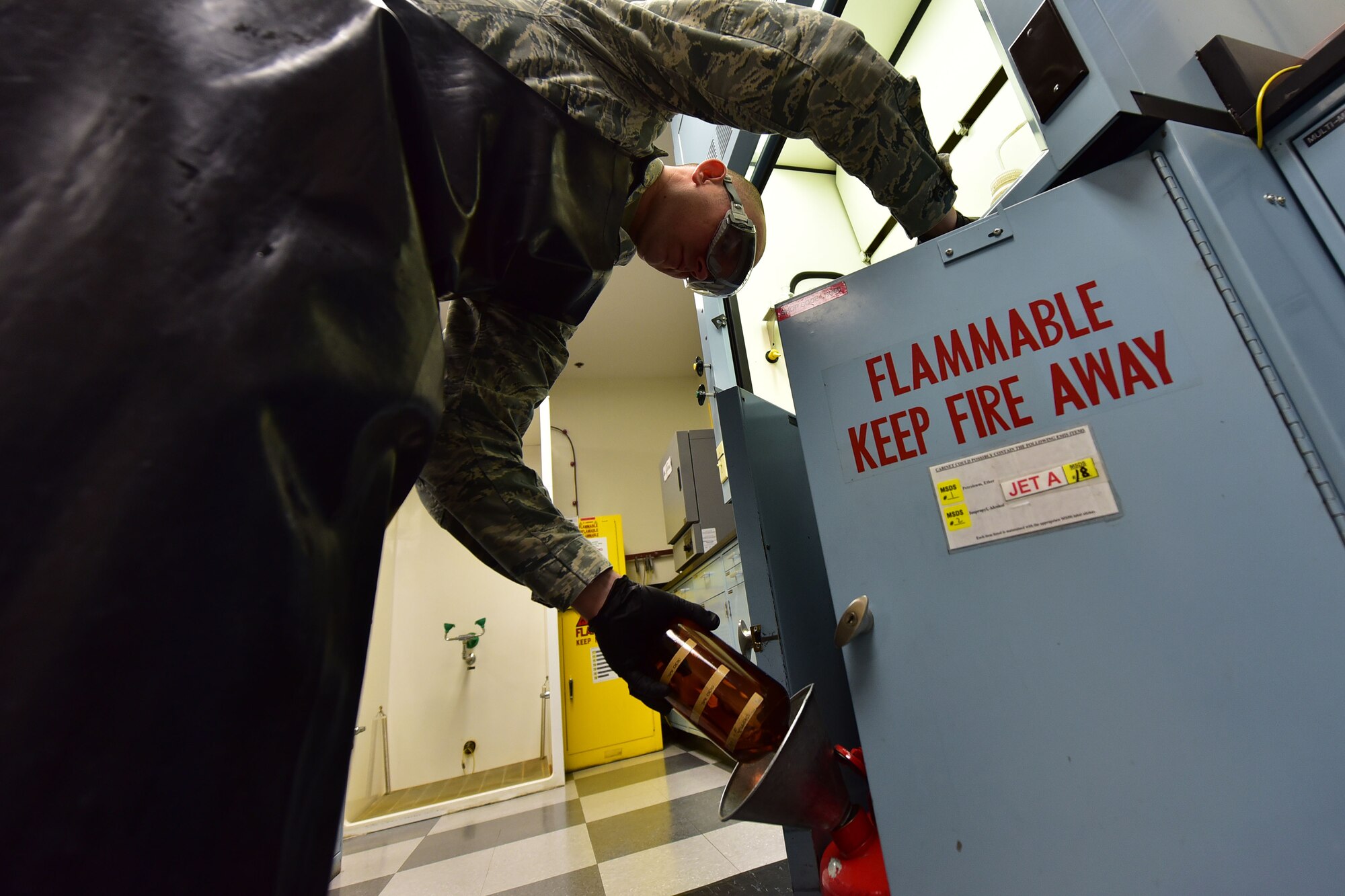 man in protective equipment dumps glass bottle of used fuel into collection container for disposal