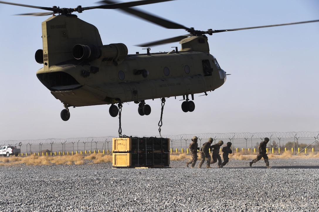 Soldiers scamper away after hooking up a pallet of supplies to a CH-47 Chinook helicopter during slingload operation.