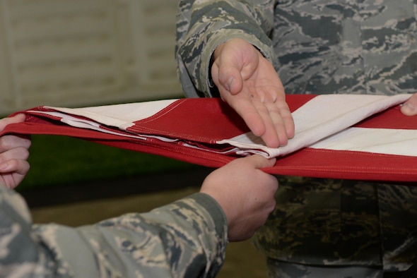 Airman 1st Class Joseph Serrano, a material management specialist assigned to the 28th Logistics Readiness Squadron, presents the first fold of a flag during an honor sequence at the Pride Hangar at Ellsworth Air Force Base, S.D., Oct. 26, 2017. The flag folding sequence entails the march-up formation, the casket carry and the flag fold itself which takes place before or after the eulogy is given. (U.S. Air Force photo by Airman Nicolas Z. Erwin)