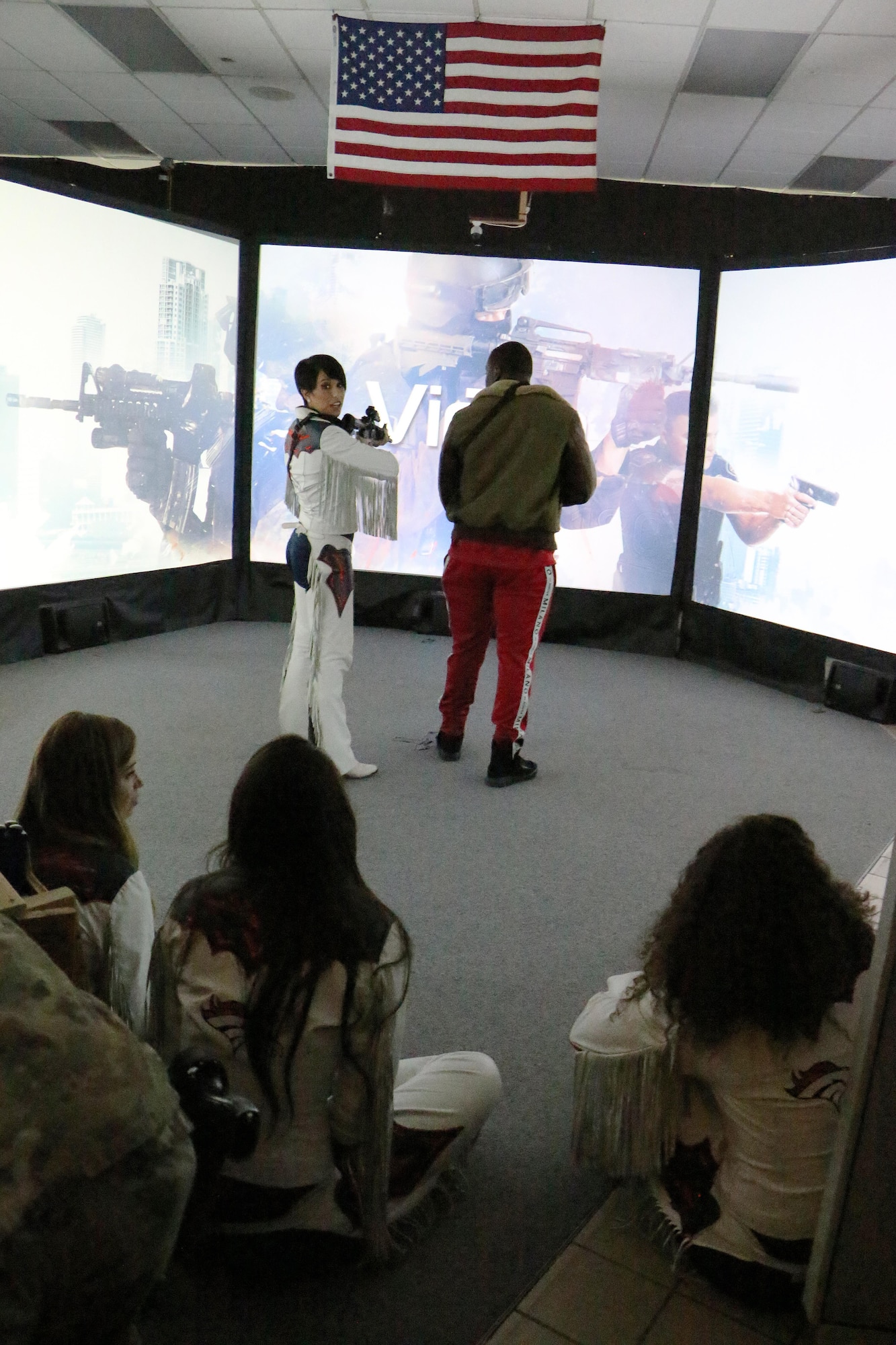 Denver Broncos cheerleader Brielle and Zaire Anderson, Denver Broncos inside linebacker, test a virtual training simulator Nov. 8, 2017 at the 21st Security Forces Squadron training facility on Peterson Air Force Base, Colorado. According to the VirTra website, the training simulator can train teams for the most difficult real-world situations, ambushes, and maintaining situational awareness during extreme stress. (U.S Air Force photo by Staff Sgt. Erica Picariello)