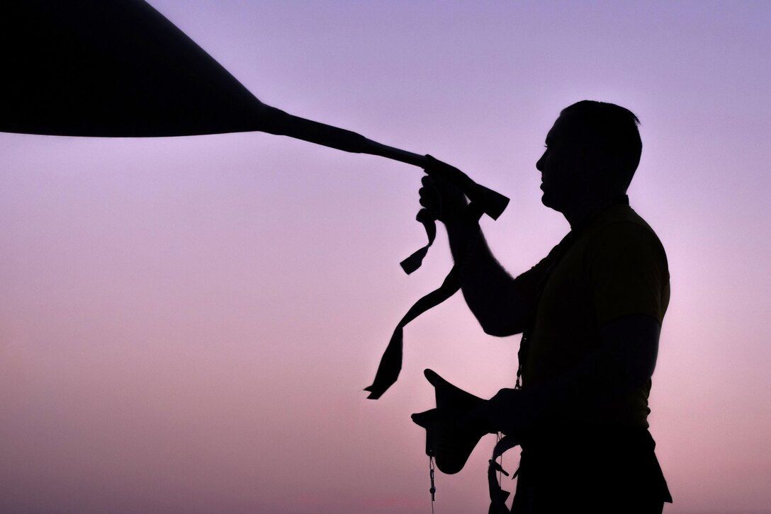 An airman, shown in silhouette, places a cover on a tube on the tip of a jet's nose, against purple sky