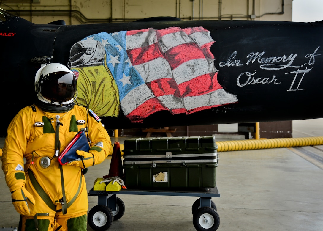 A man in a space suit stands in front of a picture of a flag