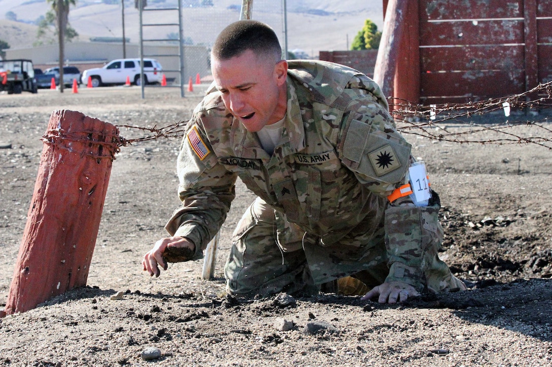 Army Sgt. Joshua Monday low crawls under the barbed wire obstacle.