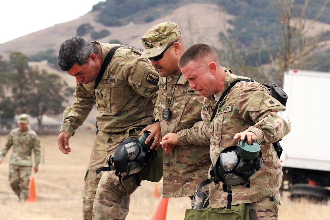 Army Staff Sgt. Francisco Vianaescobar, left, and Sgt. Joshua Monday, receive help Staff Sgt. James McBroom, a cadre, after exiting a gas chamber.