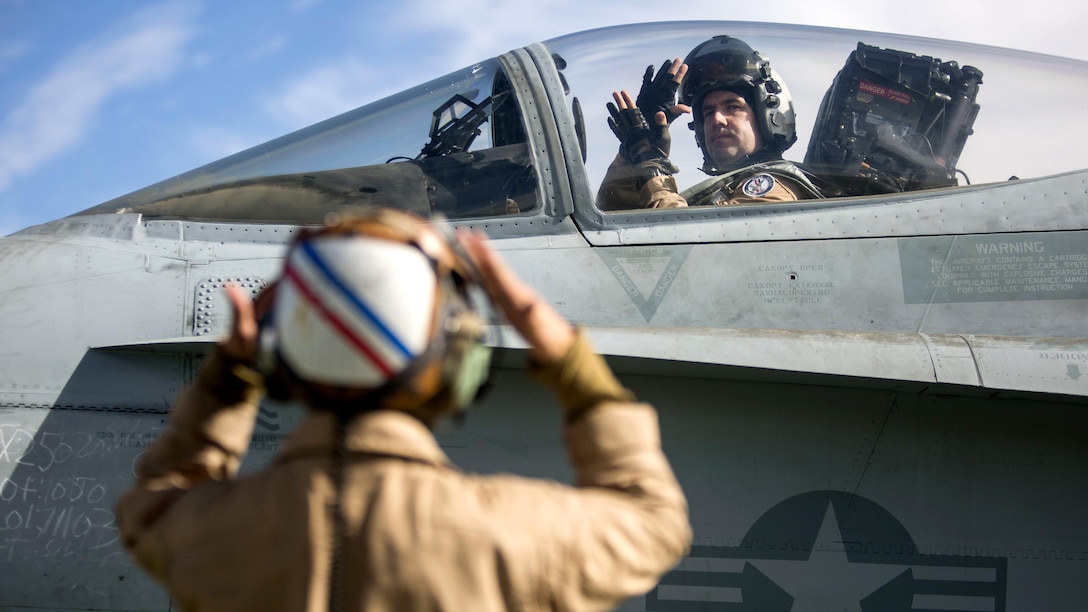 A pilot in an aircraft and a crew member signal to one another.