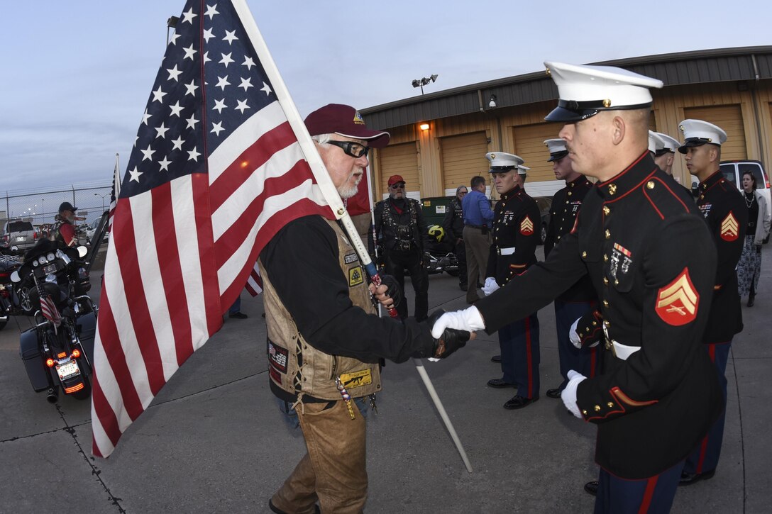 Phil Lutes, an Oklahoma Patriot Rider, carries an American flag while shaking the hand of Marine Corporal David Korn, electro-optical ordnance repair technician, prior to the remains of Marine Corps Pvt. Vernon Paul Keaton arriving in Oklahoma November 14, 2017, Will Rogers World Airport, Oklahoma City, Oklahoma.