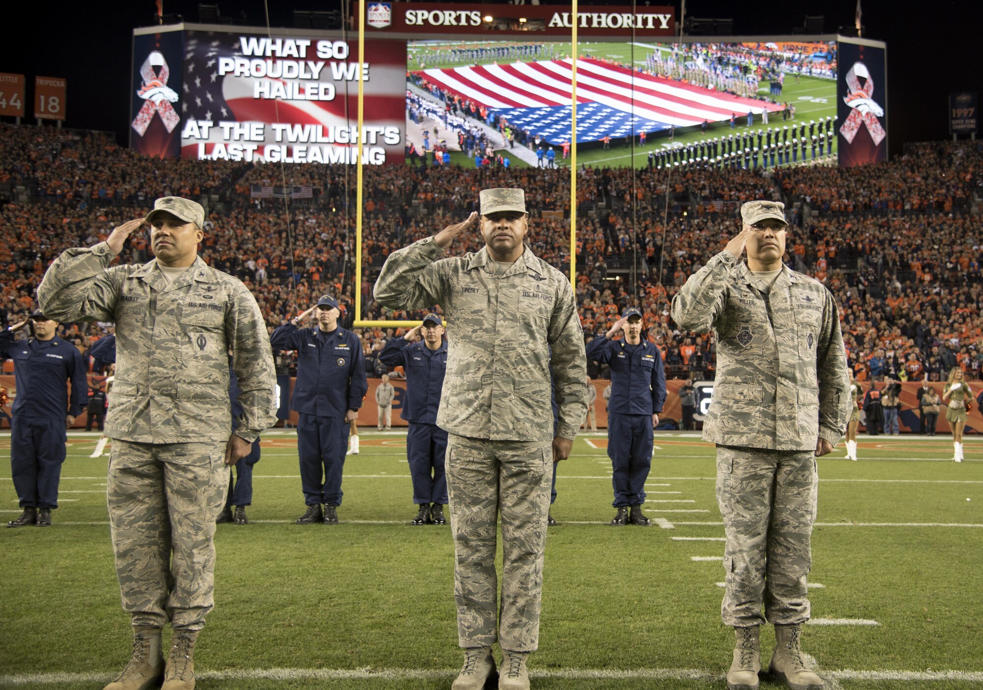 From left to right: Col. Lorenzo “Che” Bradley, 460th  Operations Group commander, Chief Master Sgt. Rod Lindsey, 460th Space Wing command chief, and Col. David Miller, Jr., 460th Space Wing commander, salute the American flag during the singing of the National Anthem Nov. 12, 2017, at Sports Authority Stadium at Mile High in Denver.