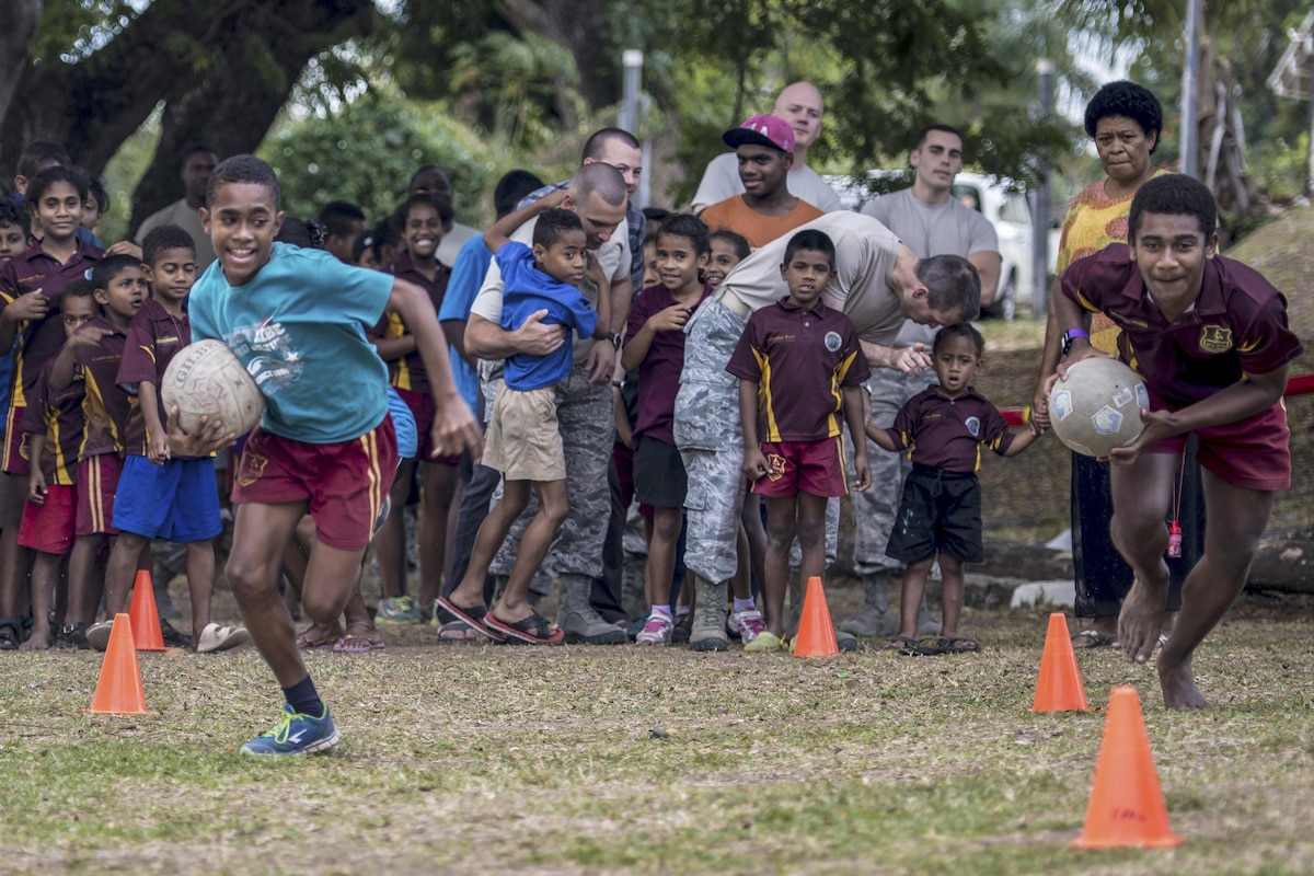 Two Fijian boys hold soccer balls as they race in front of a crowd.