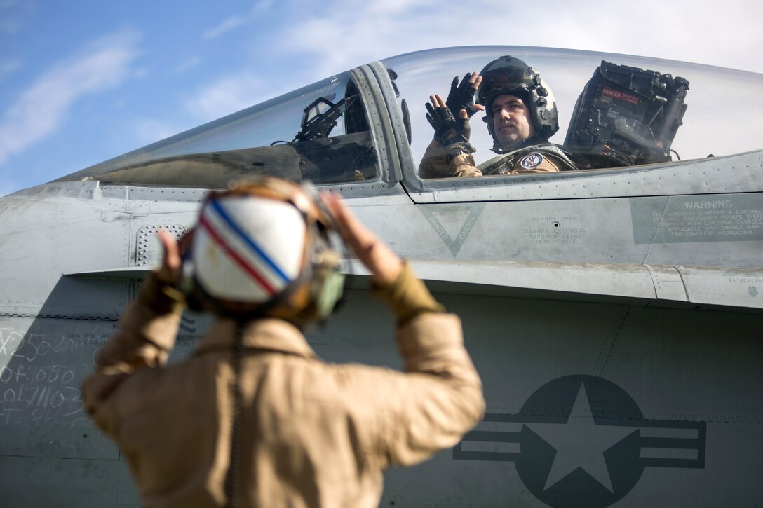 A pilot in an aircraft and a crew member signal to one another.