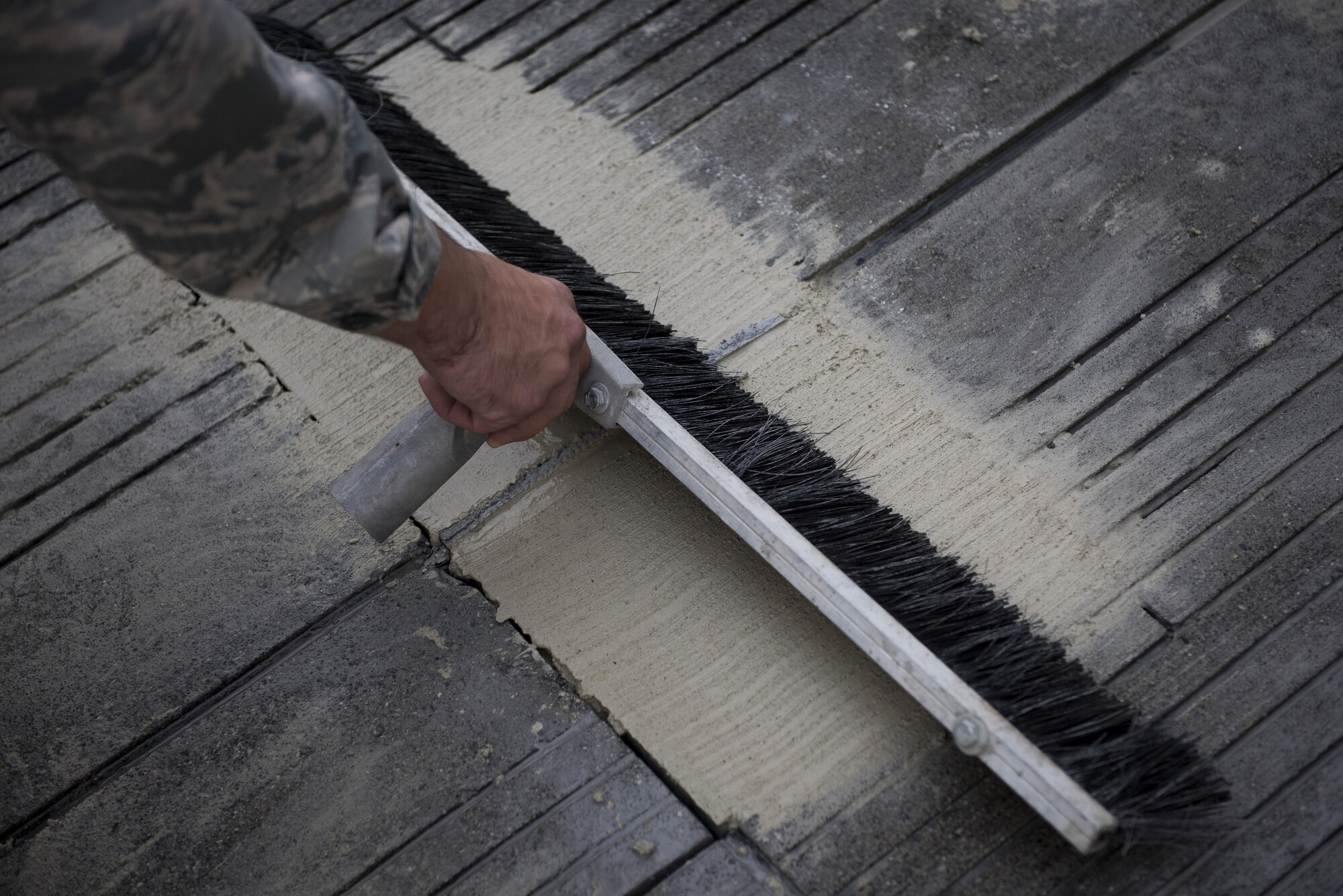 Senior Airman Brendan Kinser, 374th Civil Engineer Squadron pavements and equipment journeyman, brushes newly placed concrete on the runway, Nov. 15, 2017, at Yokota Air Base, Japan.