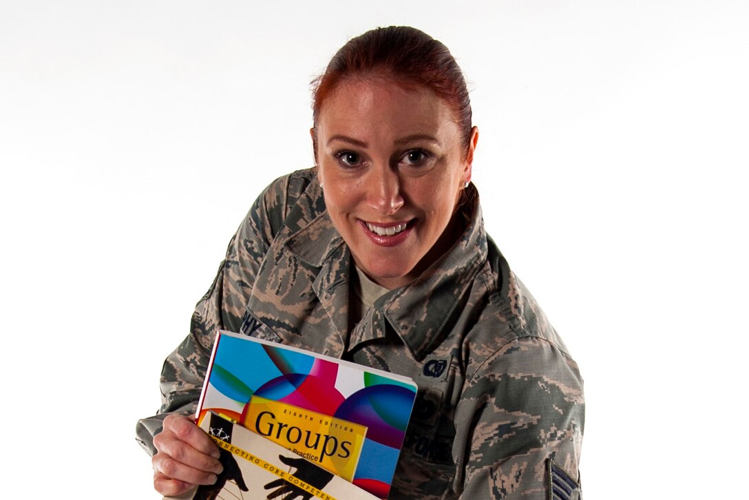 An airman poses for a photo holding some magazines.