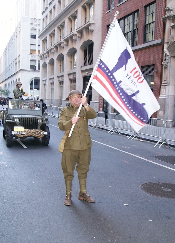 A Soldier from the 77th Sustainment Brigade carries his unit's centennial flag, commemorating 100 years since World War I, at the New York City Veterans Day Parade Nov. 11, 2017. He wears a Doughboy uniform, representing "the war to end all wars."