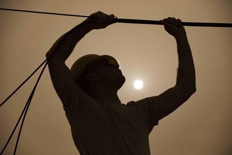SrA Jacob Ferreira, assigned to the 332nd Expeditionary Communications Squadron, clamps copper wire between rooftops as part of a base-wide wireless internet improvement project Nov. 13, 2017 in Southwest Asia. 332nd ECS took on the project with the aim of providing service members deployed in austere conditions with a safe, reliable connection to loved ones back home. (U.S. Air Force by Senior Airman Joshua Kleinholz)