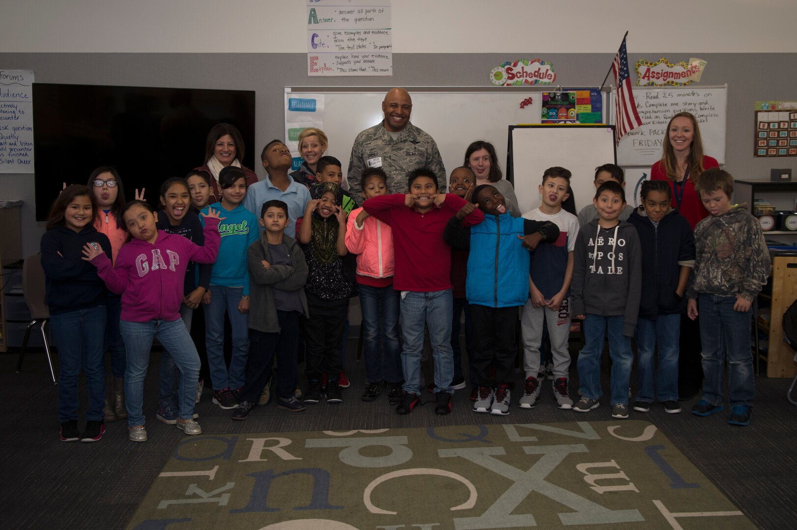 Chief Master Sgt. Rod Lindsey, 460th Space Wing command chief, his wife, Stacy, and Christine Criswell, wife of Chief Master Sgt. Brendan I. Criswell, Command Chief Master Sergeant, Air Force Space Command, pose for a photo with students at Edna and John W. Mosley P-8 School Nov. 9, 2017, in Aurora, Colo.