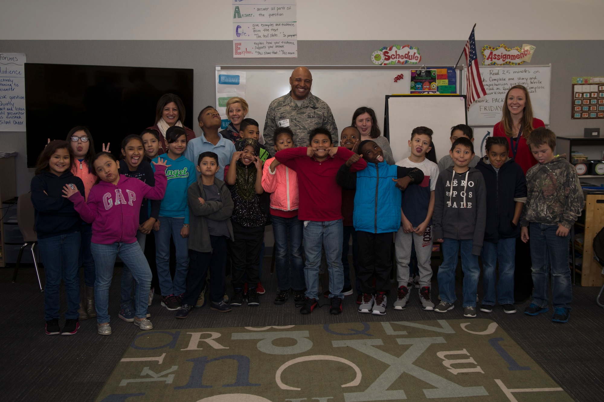 Chief Master Sgt. Rod Lindsey, 460th Space Wing command chief, his wife, Stacy, and Christine Criswell, wife of Chief Master Sgt. Brendan I. Criswell, Command Chief Master Sergeant, Air Force Space Command, pose for a photo with students at Edna and John W. Mosley P-8 School Nov. 9, 2017, in Aurora, Colo.