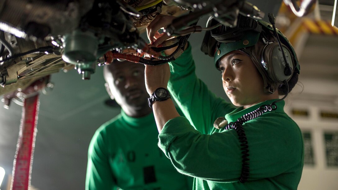 A sailor handles wiring on an aircraft.