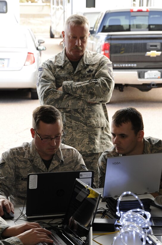 Senior Master Sgt. Robbie Engevold, the 302nd Communications Flight superintendent, looks on as Senior Airman Stephen Morrison, left, a 302nd CF cyber operations technician,  , and Tech. Sgt. Raymond Shaw, NCO in charge of cyber transport technicians, take on a coding challenge during a "Capture the Flag" cyber operations challenge at Peterson Air Force Base, Colo., Nov. 4, 2017. Members of the 302nd Communications Flight took part in the "Capture the Flag" cyber operations challenge during the November Unit Training Assembly, which aimed to test their ability to identify and respond to cyber threats in a simulated environment.. (U.S. Air Force photo/1st Lt. Stephen J. Collier)