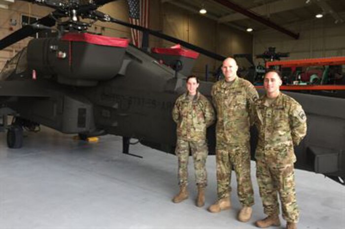 Three soldiers stand in front of a helicopter.