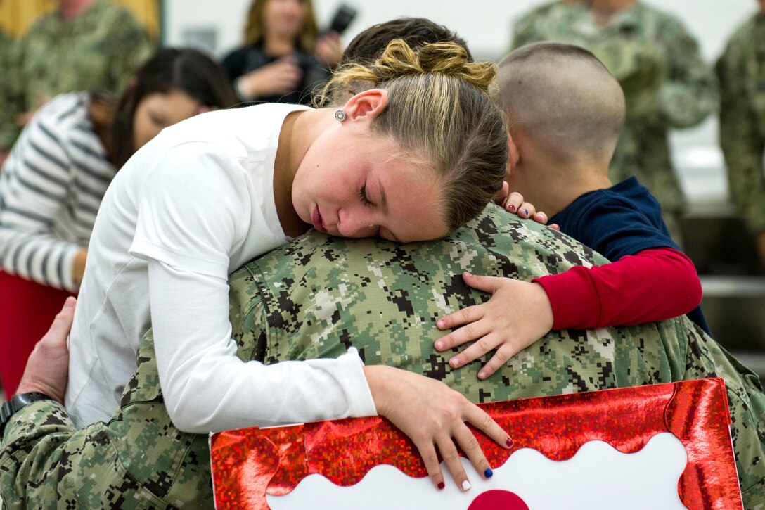 A girl cries and hugs her father, who is shown from behind as he holds her.