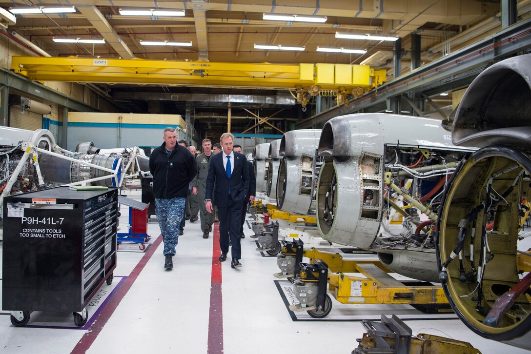 Deputy Defense Secretary Pat Shanahan walks with other personnel in a large room with aircraft parts.