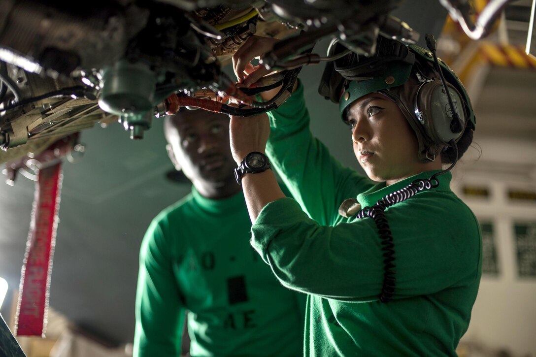 A sailor handles wiring on an aircraft.