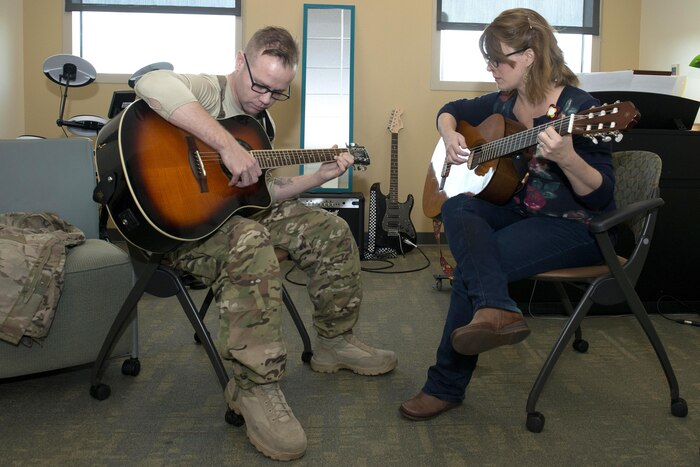 Two people sit and play guitars.