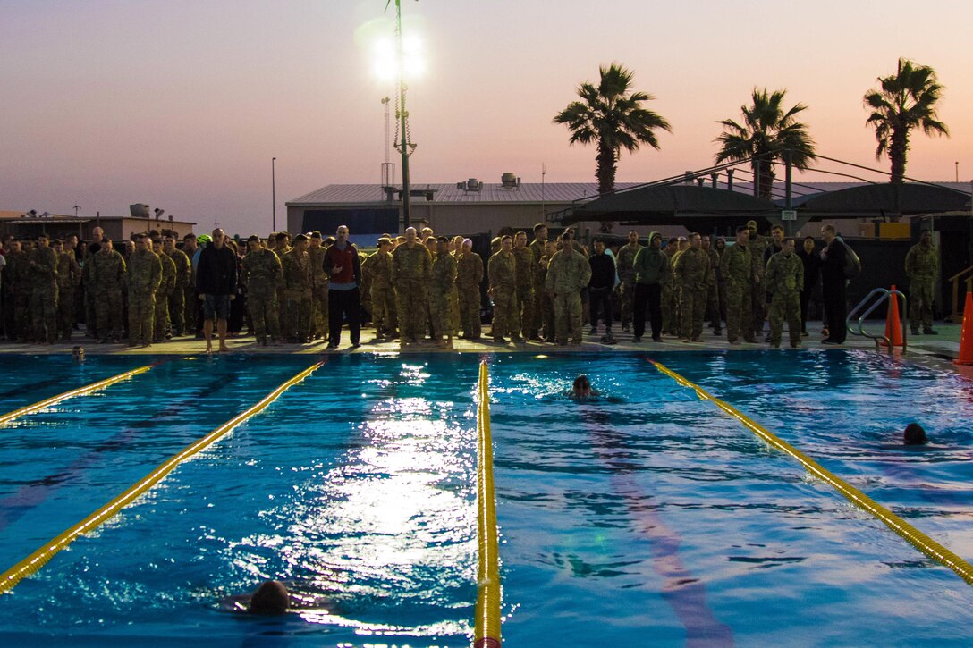 Soldiers stand around the edge of a pool while some swim.
