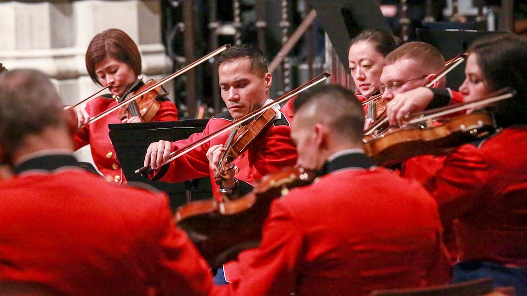 Marines in red uniforms play violins inside a cathedral.