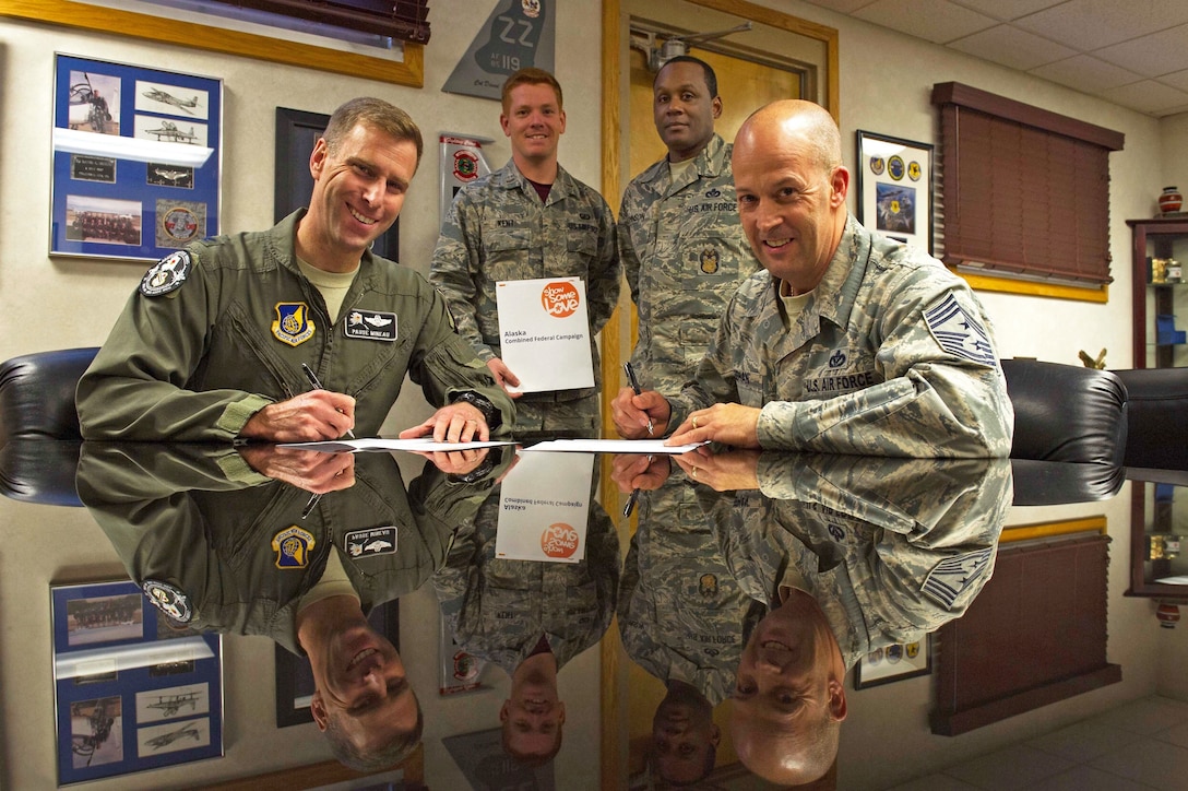 Two airmen sit at a table while two others stand in the background.