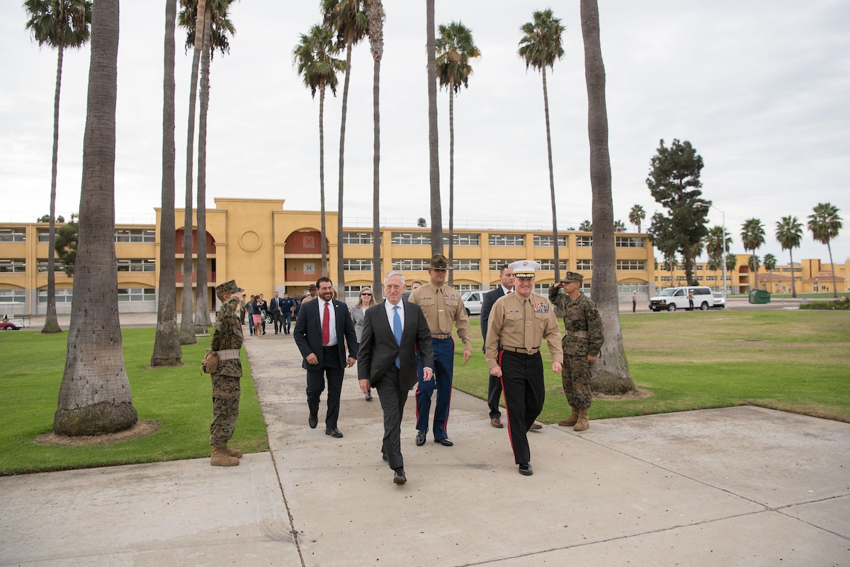 Defense Secretary Jim Mattis walks with a group of people while two Marines salute.