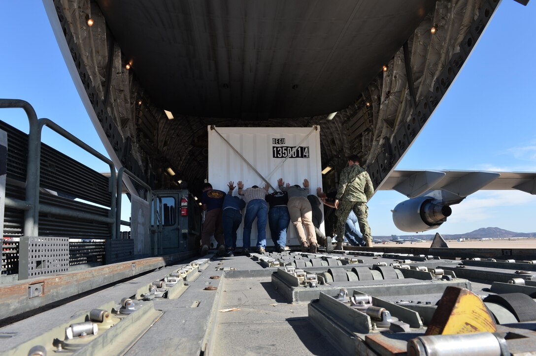 People push a container onto a cargo plane.