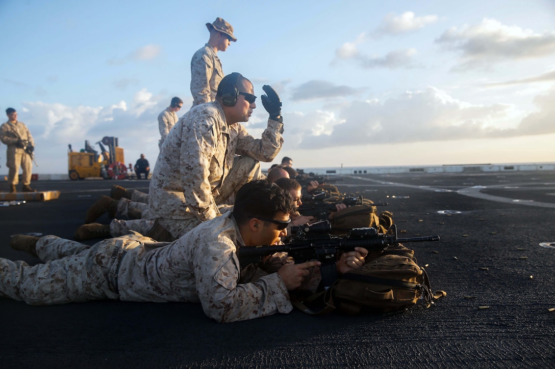 Marines lay down and kneel on the deck of a ship.