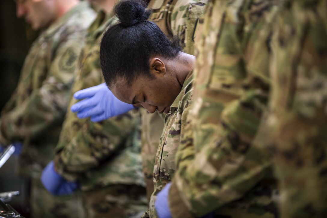A soldier bows her head while standing in a line with other soldiers.