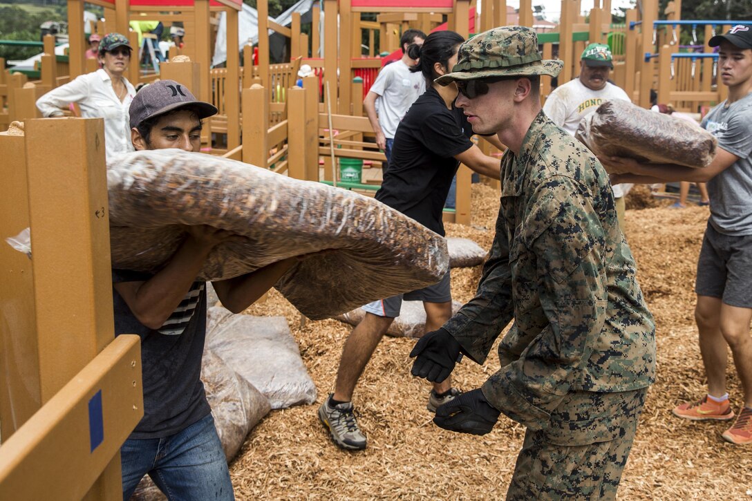 Cpl. Thomas Price helps pass on a bag of wood chips to local community volunteers during a construction project at Kamuela, on the island of Hawaii, Oct. 28, 2017. Price is a field radio operator with Combat Logistics Battalion 3, and a native of Denver, Colo. U.S. Marines with CLB-3 are helping rebuild a local community playground alongside volunteers from Kamuela. (U.S. Marine Corps photo by Lance Cpl. Isabelo Tabanguil)